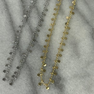 May include: Two delicate necklaces with a chain design and small round charms. One necklace is silver and the other is gold.