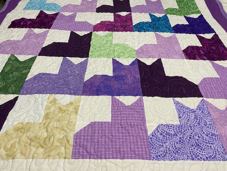 May include: Purple, green, and blue patchwork quilt with a cat design. The quilt is made of various fabrics with different patterns and textures.