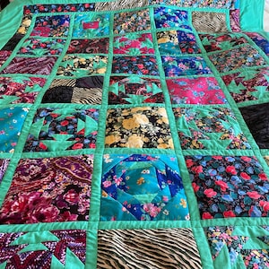 May include: A teal and green patchwork quilt with a variety of floral and geometric patterns. The quilt is made up of squares and rectangles, and the seams are visible.