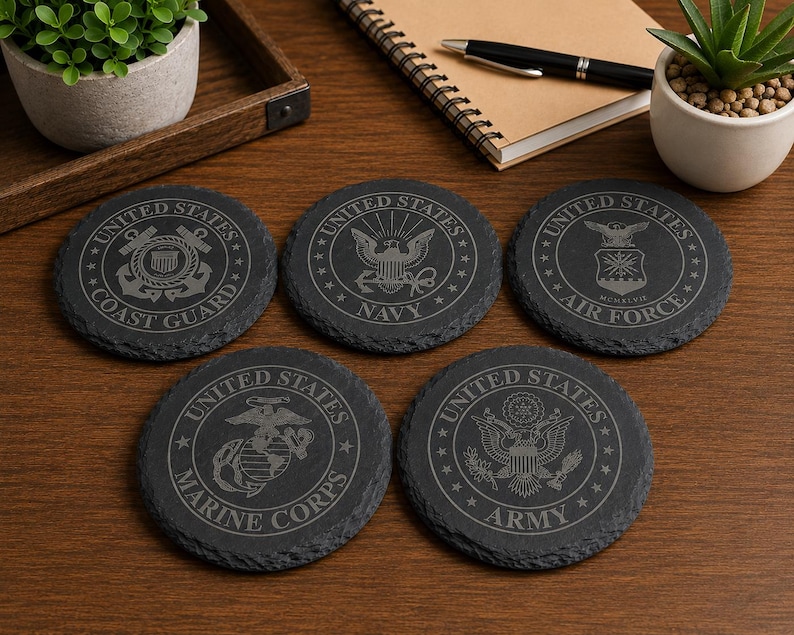 May include: Five dark grey slate coasters, each with a different etched emblem of a United States military branch. The coasters display the Coast Guard, Navy, Air Force, Marine Corps, and Army insignias, ideal for drinks.