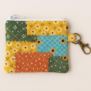 May include: A patchwork coin purse with a white zipper and a bronze-colored clasp. The purse is made of fabric squares in various colors, including yellow with white flowers, blue with sunflowers, green with white dots, and orange.