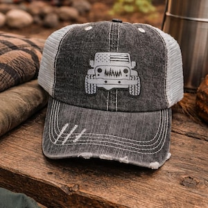 May include: A distressed black and white trucker hat with a graphic of a jeep and an American flag design. The hat has a mesh back and a curved brim. The hat is sitting on a wooden surface.