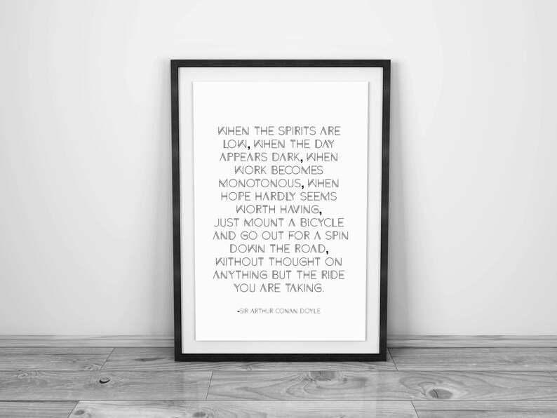 May include: A framed print with a black border, featuring a quote by Sir Arthur Conan Doyle. The quote is in black text on a white background. The print is leaning against a wall on a wooden floor.