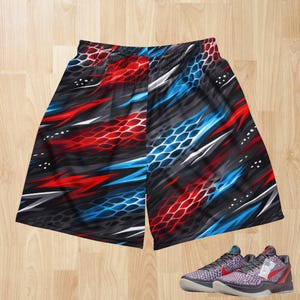 Puede incluir: Pantalones cortos de baloncesto negros con un diseño abstracto rojo, blanco y azul. Los pantalones cortos tienen una cintura elástica. Un par de zapatillas de baloncesto a juego con detalles en rojo están en la parte inferior de la imagen.