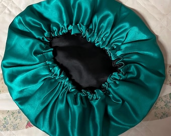 Può includere: Un cappuccio in raso verde acqua con interno nero. Il cappuccio è raccolto sul bordo con un elastico. Il tessuto ha una consistenza lucida e liscia. Il cappuccio è progettato per proteggere i capelli durante il sonno.