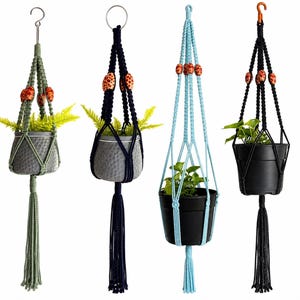 Puede incluir: Cuatro colgadores de plantas de macramé con cordones anudados y borlas. Dos colgadores presentan cordones verde salvia y azul marino con cuentas de madera naranja estampadas, mientras que los otros son azul claro y negro, con cuentas naranja.