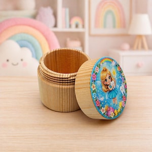 Op de afbeelding: Een houten tandenfee-doosje met een deksel met een cartoonfee die een tand vasthoudt. De doos is gemaakt van lichtgekleurd hout en heeft een ronde vorm. Het deksel is versierd met een kleurrijke illustratie van een fee, bloemen en een regenboog.