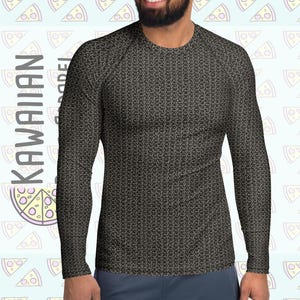 Puede incluir: Una camiseta de manga larga negra y gris con un patrón de cota de malla repetido. La camiseta lleva la marca "KAWAIIAN APPAREL" y un logotipo de una porción de pizza. El fondo presenta un patrón azul claro de porciones de pizza.