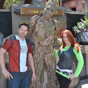 Könnte beinhalten: Zwei Personen, die als Charaktere aus der Guardians of the Galaxy-Filmreihe verkleidet sind, posieren mit einem Kostümcharakter, der Groot aus demselben Film darstellt. Der Hintergrund zeigt ein Schild mit der Aufschrift "Tivan Collection".