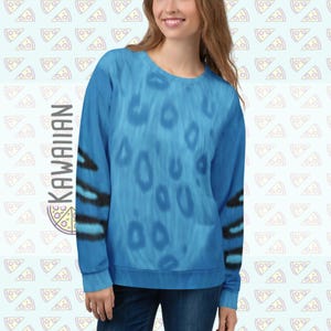 May include: A blue sweatshirt with a pattern of large, lighter blue spots. The sleeves have black and blue stripes. The word "KAWAIIAN" is printed vertically on the left side of the sweatshirt. The background has a repeating pattern of pizza slices.