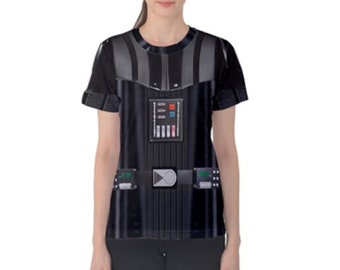 Puede incluir: Camiseta negra con una imagen impresa de Darth Vader de Star Wars. La camiseta tiene un fondo negro con una imagen detallada del icónico traje de Darth Vader, incluyendo su casco, pieza de pecho y cinturón.