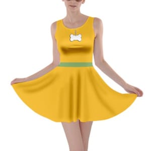 Puede incluir: Un vestido amarillo sin mangas con una cintura verde y un dije de hueso blanco en la parte delantera. El vestido tiene una falda acampanada.