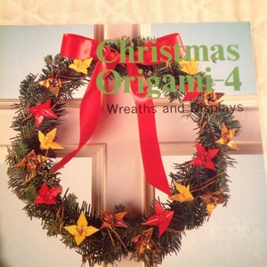 May include: A book titled "Christmas Origami-4 Wreaths and Displays" with a red ribbon and a wreath made of green branches and origami stars in red and gold.