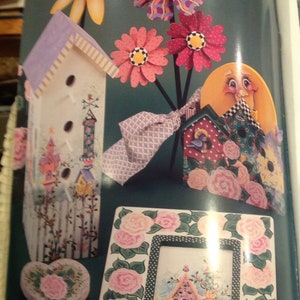 May include: A collection of hand-painted wooden birdhouses with floral and whimsical designs. The birdhouses are decorated with flowers, polka dots, and other patterns. There is a heart-shaped birdhouse with a pink and green floral design, a birdhouse with a purple roof and a white body, and a birdhouse with a red roof and a white body. The birdhouses are all on a green background.