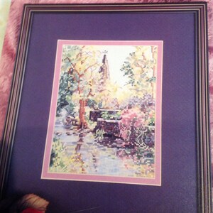 Puede incluir: Un patrón de punto de cruz enmarcado de un campanario de iglesia con un jardín colorido en primer plano. El título del patrón es "Marty Bell Overbrook Steeple".