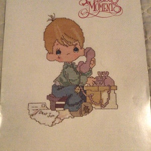 May include: Cross stitch pattern featuring a Precious Moments character, a young boy, sitting on a chair and talking on a phone. The pattern is titled "Dear Jon" and is from book PM-3.