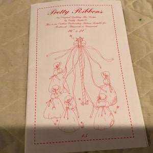 May include: A vintage embroidery pattern booklet titled "Pretty Ribbons" by Cathy Parker. The pattern features a maypole with five girls dancing around it. The booklet is 16 inches by 21 inches and is numbered #5.