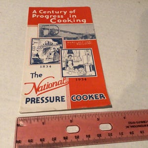 May include: A vintage pamphlet titled "A Century of Progress in Cooking" with illustrations and text. The cover is red and white, featuring the words "The National Pressure Cooker." A pink ruler is at the bottom.