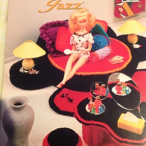 May include: A crochet dollhouse furniture set featuring a red and black sofa, a vanity with a mirror, a stool, and a lamp. The set is designed for a dollhouse and is made of yarn.