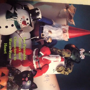 May include: A book titled "Let's Paint Pot Bellies" by Jane Dillon. The book cover features a variety of colorful, hand-painted characters, including a snowman, a gnome, a Santa Claus, a black cat, and a pumpkin. The book is part of the Sis and Sons Presents series.