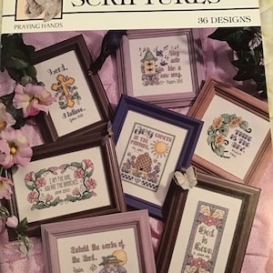May include: A collection of 36 cross-stitch patterns featuring religious verses and images. The patterns are framed in various colours and include verses such as "God is Love", "I am the vine, you are the branches", and "Behold the works of the Lord."