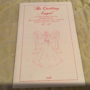Peut inclure: Un patron de couture blanc pour quilting avec un dessin au trait d'un ange avec des ailes. Le patron est intitulé "The Quilting Angel" et mesure 16 pouces par 21 pouces. Le numéro du patron est #40.
