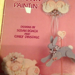 May include: A book cover with the title "Uptown Paintin'" by Susan Roach and Emily Dinsdale. The cover features a pink background with illustrations of a pig, a bunny, and a heart-shaped decoration.
