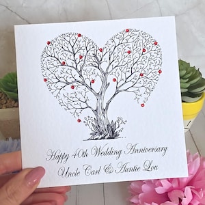 Puede incluir: Una tarjeta de felicitación cuadrada de color blanco con una ilustración en tinta negra de un árbol cuyas ramas forman un corazón. Pequeñas cuentas rojas están adheridas a las ramas. El texto dice Happy 40th Wedding Anniversary Uncle Carl & Auntie Lou.