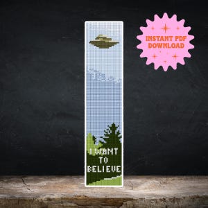 Könnte beinhalten: Ein Kreuzstich-Lesezeichen mit einem UFO, das über einen Wald fliegt, mit dem Text "I WANT TO BELIEVE".