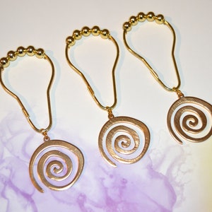 May include: Three gold shower curtain rings with a spiral design. Each ring has a chain of small gold beads.