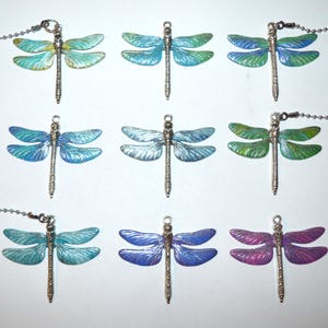 May include: Nine dragonfly pendants in various colors, including blue, green, and purple. Each dragonfly has a silver-colored body and wings with iridescent color gradients. The pendants are attached to a silver-colored chain.