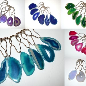May include: A collection of shower curtain rings featuring polished agate slices in various colors, including purple, blue, green, pink, and light blue. Each ring has a silver-toned metal loop and a beaded bar for hanging.