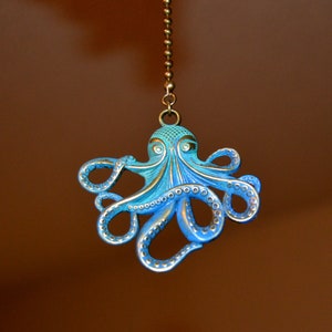 May include: A blue and turquoise octopus ceiling fan pull with a bronze chain. The octopus has detailed tentacles and a textured head. The pull hangs against a brown background.