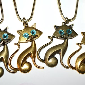 May include: Four gold-colored cat keychains with turquoise blue rhinestone eyes. Each keychain features a stylized cat design with a curled tail.