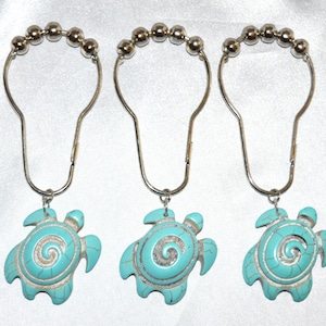 May include: Three silver shower curtain rings with turquoise blue turtle charms. Each turtle has a white swirl design.