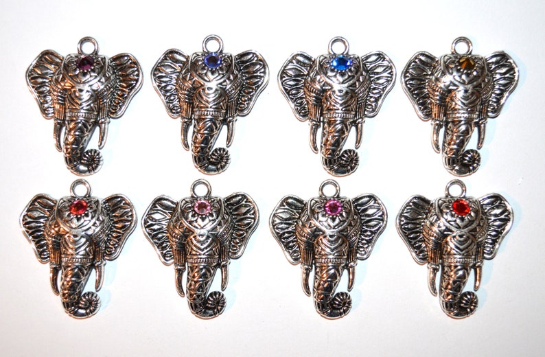 May include: Eight silver-toned elephant pendants with varying colored gemstone accents. Each pendant features detailed trunk and ear designs, and a loop for attaching to a necklace or bracelet. Gemstone colors include purple, blue, orange, and red.