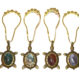 May include: Four decorative shower curtain hooks with a turtle design. Each hook features a gold-colored metal frame and a turtle pendant with a gemstone center in shades of green, brown, and purple.