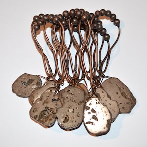 May include: Set of eight shower curtain rings with a copper finish. Each ring is adorned with a unique, irregularly shaped, light brown and gold stone.