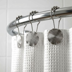 May include: A set of silver-colored shower curtain hooks with a spiral design, hanging from a curved, polished metal rod. The hooks are holding up a white waffle-weave shower curtain.