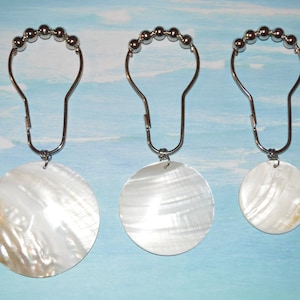 May include: Three silver shower curtain rings with white mother of pearl round ornaments attached.