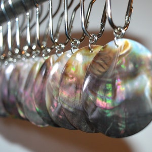 May include: A row of iridescent abalone shell earrings hanging on a silver rack. The earrings are round and have a natural, organic look.
