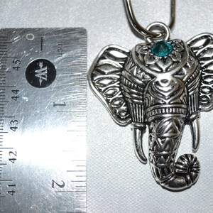 May include: Silver-toned elephant pendant with intricate detailing, a teal-colored gem, and a loop for hanging. The pendant is approximately 1.75 inches in length, showcasing a detailed design. The elephant's trunk is curled, and the ears are adorned with patterns.