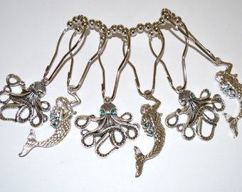 Puede incluir: Un juego de seis ganchos para cortina de ducha de metal plateado con dijes alternados de pulpo y sirena. Cada dije está detallado con pequeños diamantes de imitación de color verde azulado incrustados y unido a anillos circulares.