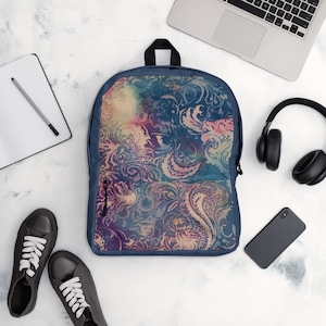 Puede incluir: Una mochila azul marino con un colorido diseño de cachemira. La mochila tiene un bolsillo frontal con cremallera y un asa superior negra. El diseño presenta remolinos de rosa, azul y amarillo. La mochila está rodeada de zapatillas negras, un portátil, auriculares, un teléfono y un cuaderno.
