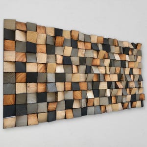 Puede incluir: Una pieza de arte mural rectangular compuesta por numerosos bloques de madera cuadrados pequeños de profundidades variables. Los bloques presentan patrones de veta de madera natural en tonos bronceado claro, marrón medio, gris oscuro y negro.