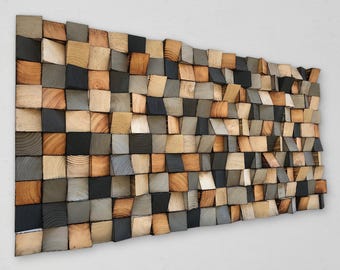 May include: A rectangular wall art piece composed of numerous small, square wooden blocks of varying depths. The blocks feature natural wood grain patterns in shades of light tan, medium brown, dark gray, and black, creating a textured surface.