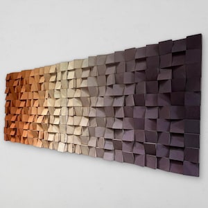 Puede incluir: Una pieza de arte mural rectangular compuesta por numerosos bloques de madera cuadrados pequeños dispuestos en una cuadrícula. Los bloques presentan un degradado de color que transita de naranja cálido a la izquierda a beige claro y morado oscuro.