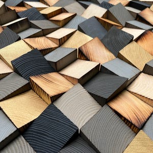 May include: A wall art piece composed of numerous small, angled wooden blocks arranged in a geometric pattern. The blocks feature a mix of natural light wood grain, charred dark wood, and solid grey finishes, creating a textured, three-dimensional surface.