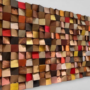 Puede incluir: Una obra de arte mural compuesta por numerosos bloques de madera en varios colores y tonos de madera. Los bloques están dispuestos para crear un efecto texturizado y tridimensional. Los colores incluyen rojo, naranja, amarillo, marrón y negro.