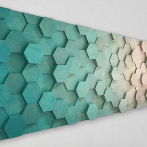 Puede incluir: Una pieza de arte de pared hecha de azulejos hexagonales de madera en tonos de verde azulado, verde y beige. Los azulejos están dispuestos en un patrón escalonado, creando un efecto texturizado y dimensional.
